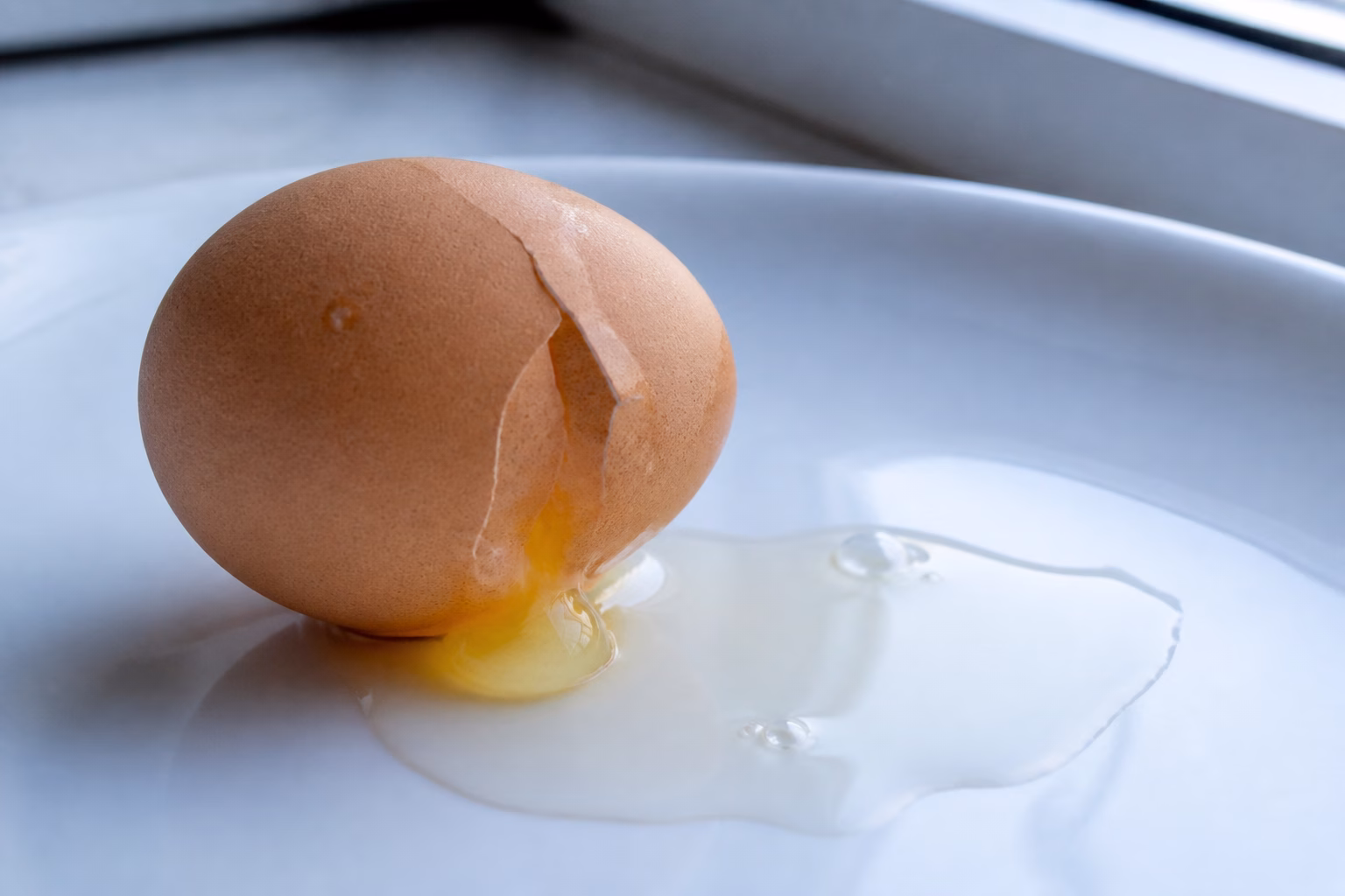 Тріснуте куряче яйце з витікаючим білком на білій поверхні